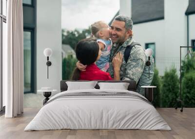 Military man hugging his wife and daughter after returning home Wall mural