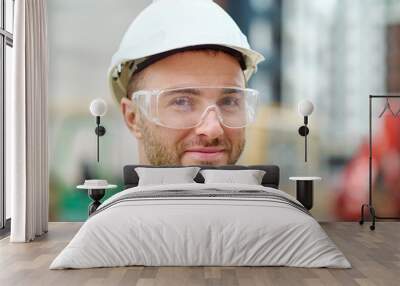 Pleased attractive builder in safety goggles posing for the camera Wall mural