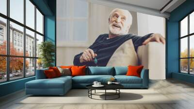 Pleasurable time. Joyful senior man smiling while enjoying his rest at home Wall mural