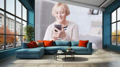 Positive minded senior lady looking at screen of her smartphone Wall mural