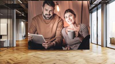 Relaxed attractive couple sitting in a room and watching a movie on the tablet Wall mural