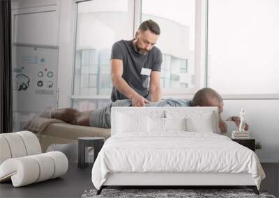 Skillful orthopedist. Skilled bearded man doing a back massage for his patient while working as an orthopedist Wall mural