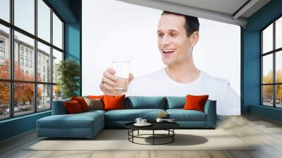 So thirsty. Cheerful delighted nice man holding a glass of water and looking at it while preparing to drink Wall mural