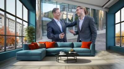 Two smiling male colleagues having friendly conversation outside, patting each other Wall mural