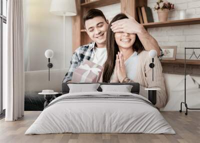 Wait a second. Cheerful male person keeping smile on his face while preparing present for his friend Wall mural