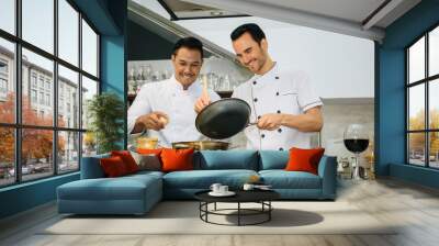 Two young chefs are preparing and cooking food at the kitchen of a restaurant Wall mural