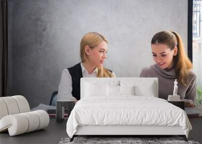 Two young european business women are sitting on the table and discussing about their work or project Wall mural