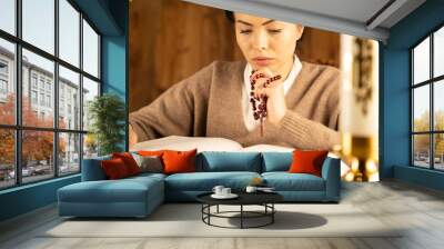 Christian woman with Bible praying in church by the altar. Woman kneeling in prayer with hands crossed keeping rosary. Wall mural