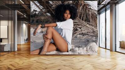 beautiful young african american girl sitting on sand at the beach Wall mural