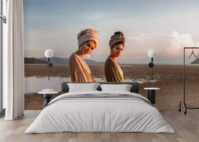 two young beautiful girls in turban walking on the beach at sunset Wall mural