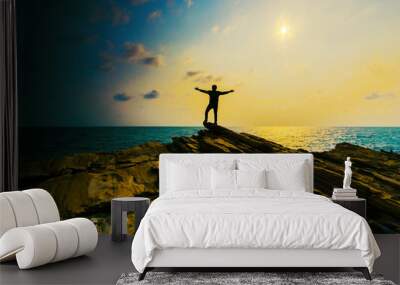 man hand up on the top stone with the sunset over sea. Wall mural