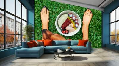 Natural dog food. Dog lying on green grass in front of its food bowl Healthy natural dog food concept Top view Wall mural