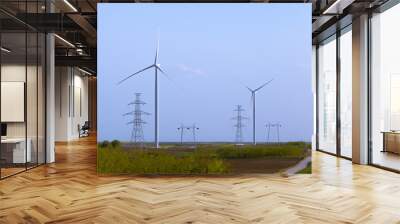 two windmill turbines on agricultural field with large electricity towers in front, blue sky in back Wall mural