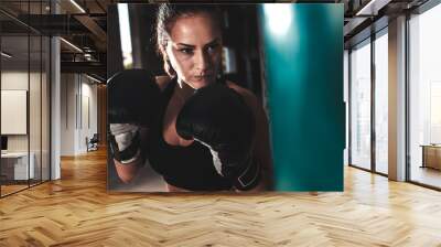 Female boxer punching a boxing bag in warehouse. Wall mural