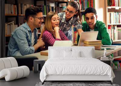 Four young students study in the school library, female student using laptop for researching online. Wall mural