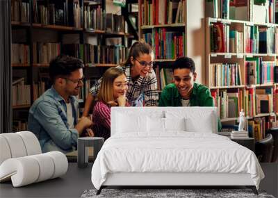 Four young students study in the school library, female student using laptop for researching online. Wall mural