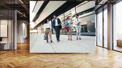 Group of coworkers walking outside in front of office buildings discuss about business plan. Wall mural