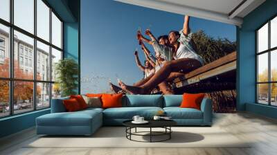 Group of friends sitting on the edge of a pier having fun and enjoying a summer day at the lake. Wall mural