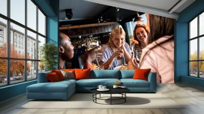 Group of young female friends having fun in restaurant, talking and laughing while dining at table. Wall mural