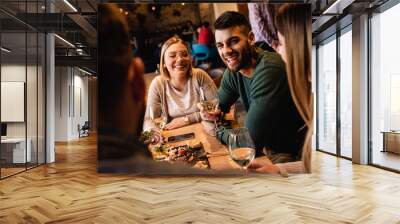 Group of young friends having fun in restaurant, talking and laughing while dining at table.	 Wall mural