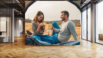 Happy young couple sitting by tent at campsite spending time together in nature looking at map for direction. Wall mural