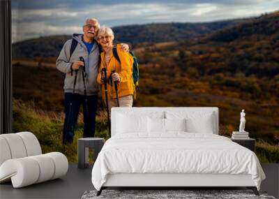 Portrait of active senior couple with backpacks hiking together in nature on autumn day. Wall mural