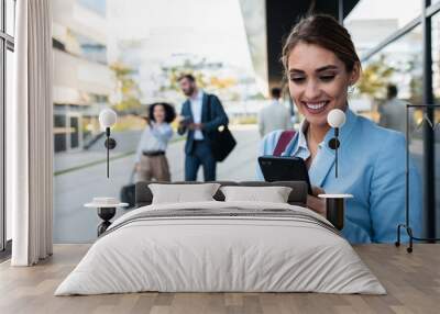 Portrait of smiling businesswoman standing in front of modern office buildings looking at phone.	 Wall mural