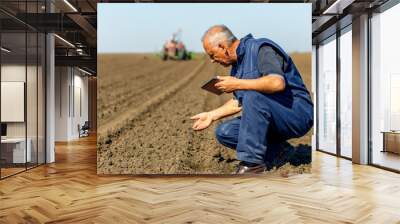 Senior farmer in field examining sowing and holding tablet in his hands. Wall mural