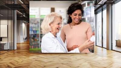 Senior pharmacist selling medications to young female customer in the pharmacy store. Wall mural