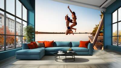 Single mother with her son enjoying on vacation jumping in lake from pier on summer day. Wall mural