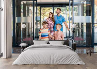 Smiling family of four enters to the hotel lobby to check in at the reception for vacation. Wall mural