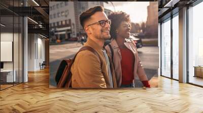 Smiling mix couple enjoying on vacation, young tourist having fun walking and exploring city street during the day. Wall mural