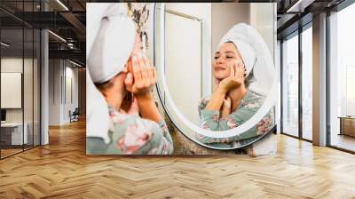 Smiling woman in her bathroom looking at herself in the mirror with satisfaction. Wall mural