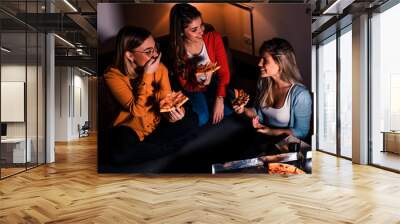 Three female friends chatting and enjoying eating pizza at home. Wall mural