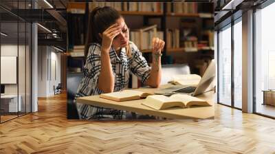 Tired young female student study in the library using laptop for researching online. Wall mural