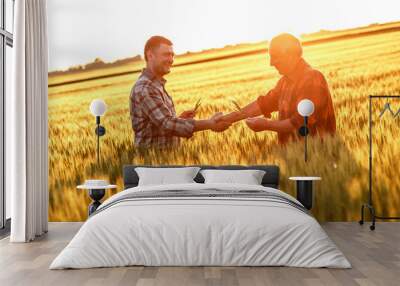 two farmer standing in a wheat field and shake hands on sunset. Wall mural