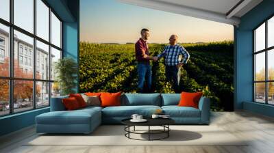 Two farmers in soy field making agreement with handshake at sunset. Wall mural