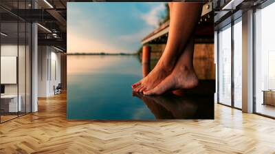 Woman legs as she sitting on wooden dock by the lake. Wall mural