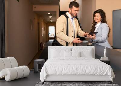 Young business man check-in in hotel, smiling female receptionist behind the hotel counter showing him available rooms on tablet. Wall mural