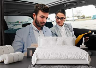 Young business people working together while traveling by a car. They are using laptop and preparing for meeting.	 Wall mural