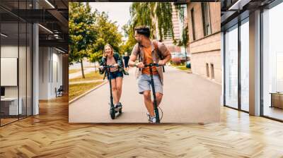 Young couple on vacation having fun driving electric scooter through the city. Wall mural