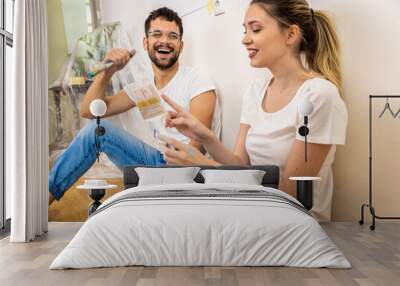 Young couple sitting on the floor choosing color for painting the wall in their home. Wall mural