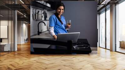 Young female nurse at home in the kitchen having video call using laptop. Wall mural