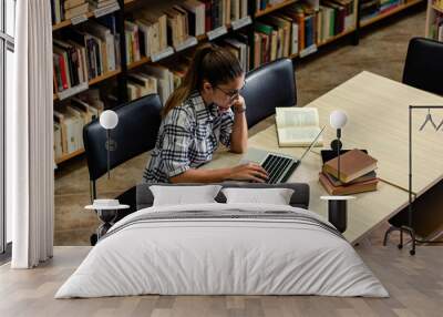 Young female student study in the library using laptop for researching online.	 Wall mural