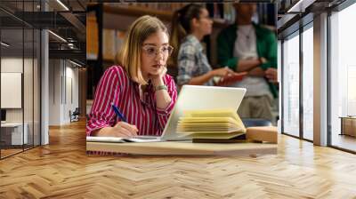 Young female student study in the library using laptop for researching online. Wall mural