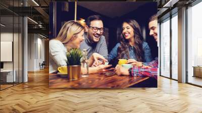 Portrait of cheerful young friends looking at smart phone while sitting in cafe. - Image Wall mural