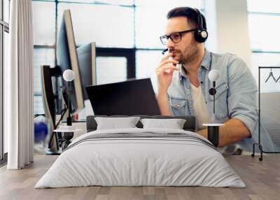 Young male call center operator working on his computer while his headset is on. Wall mural