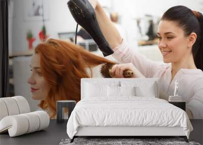 Shot of a cheerful hairdresser blow drying hair of a beautiful young woman, working at her beauty salon. Attractive young ginger haired female gitting her hair dried by a professional stylist Wall mural