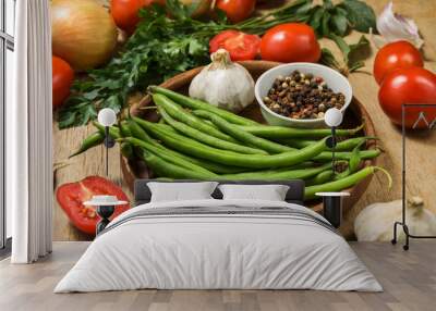 Fresh ripening vegetables on a wooden table. Zucchini, asparagus beans, tomatoes and garlic in a clay plate while preparing a vegetarian meal on the kitchen table. Wall mural