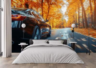 A sleek black car drives swiftly along a winding road flanked by trees showcasing brilliant autumn colors. The scene captures the essence of fall Wall mural